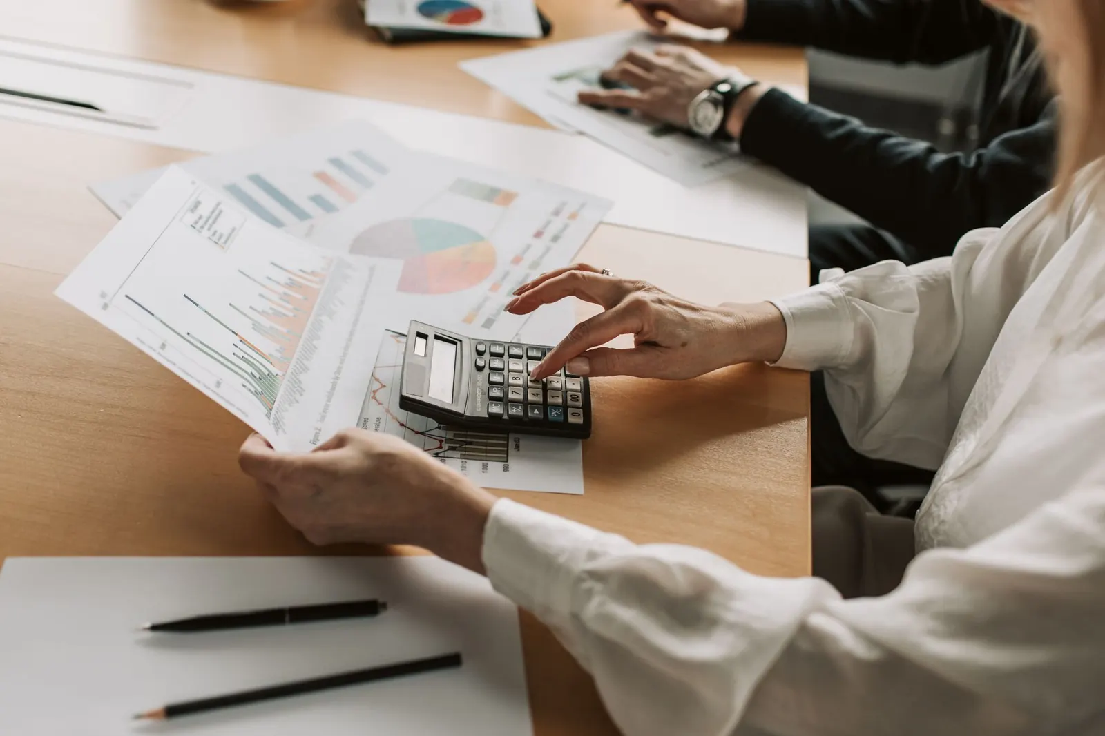 Hands working through figures on a calculator beside printed charts