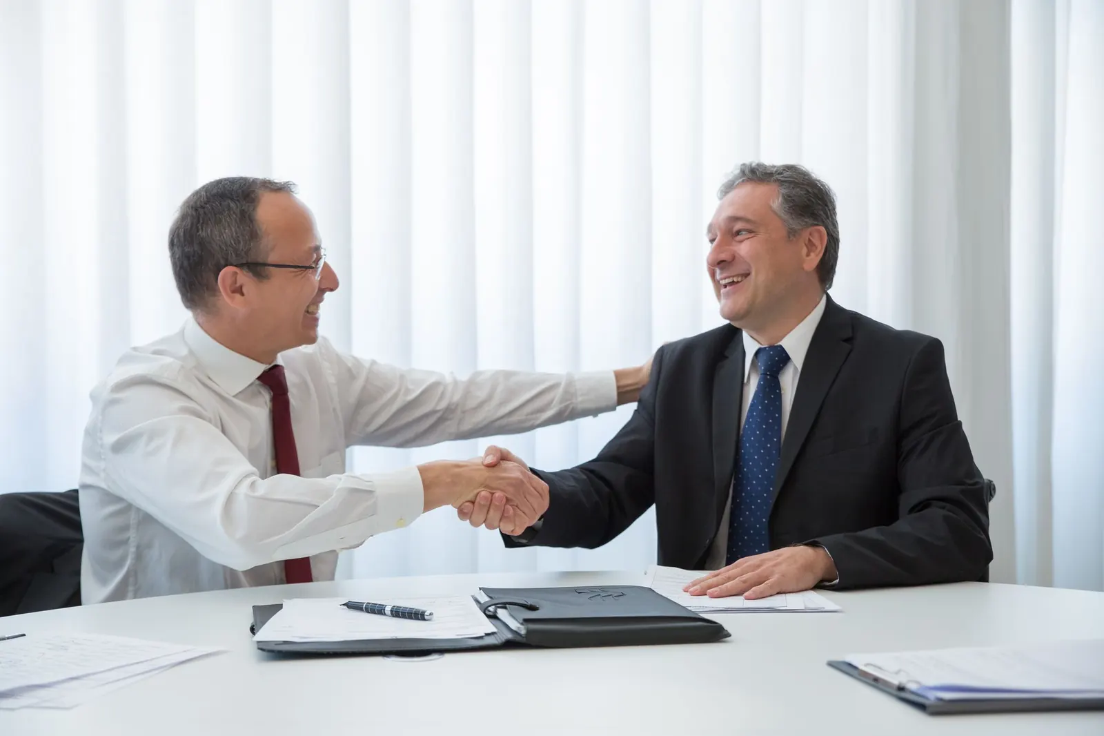 Two business partners shaking hands across a meeting table