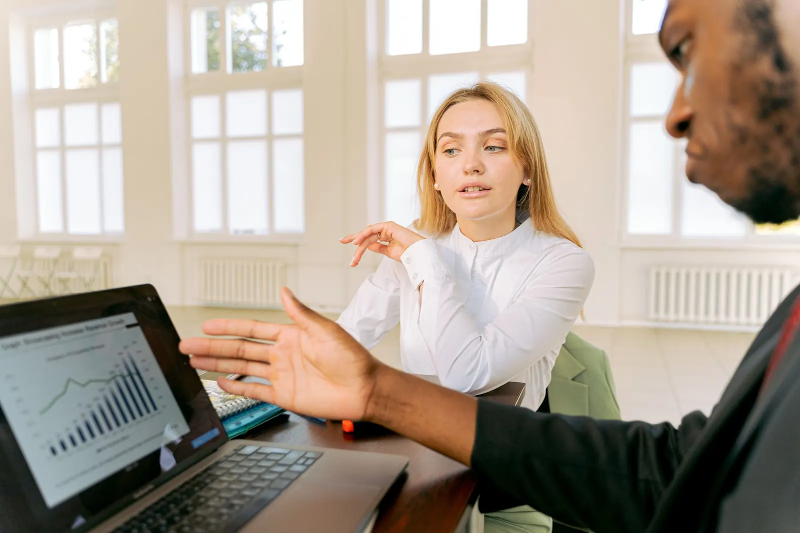 A woman explaining an idea while a colleague reviews a chart on a laptop